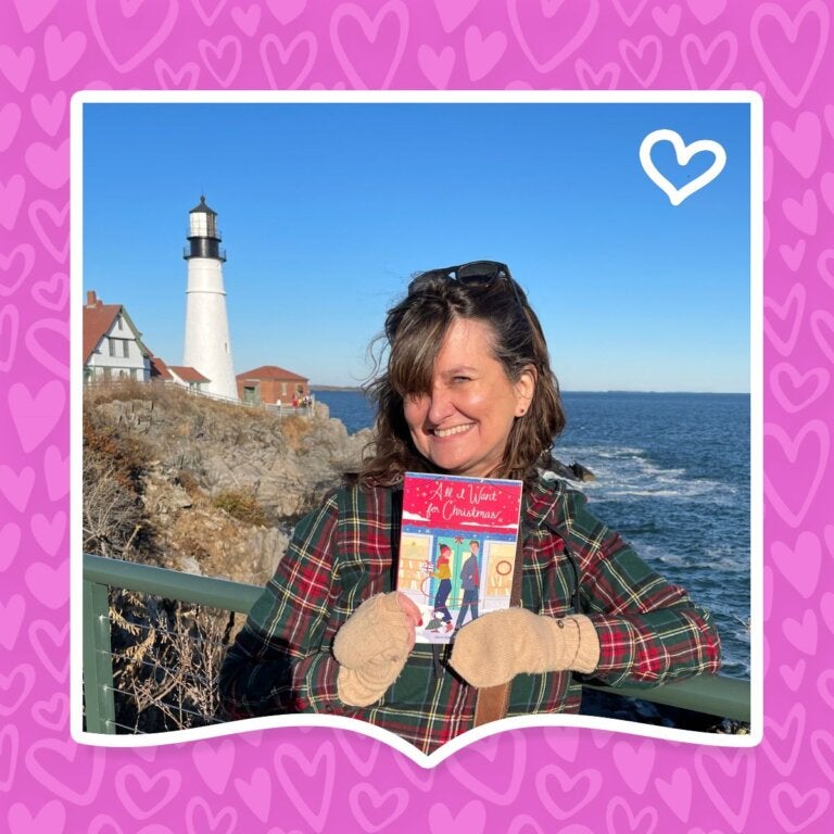 Author Wendy Loggia poses in front of a lighthouse with her book All I Want for Christmas